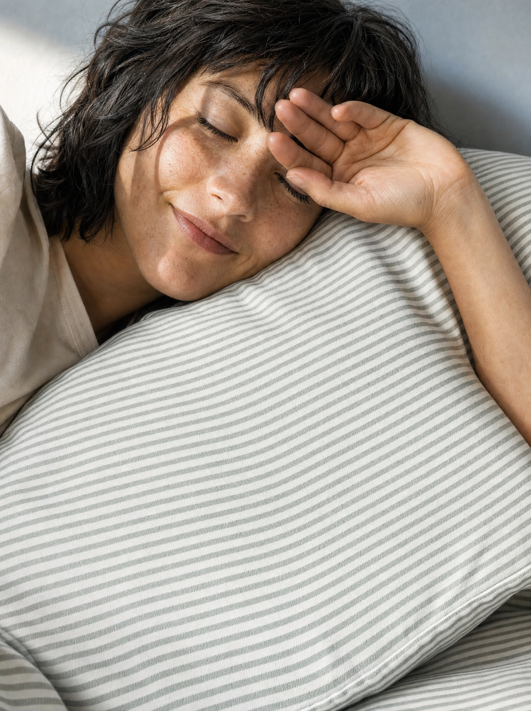 A woman rests against a fine green-and-white striped SOLFIBBLA pillow, shading her eyes from the morning light